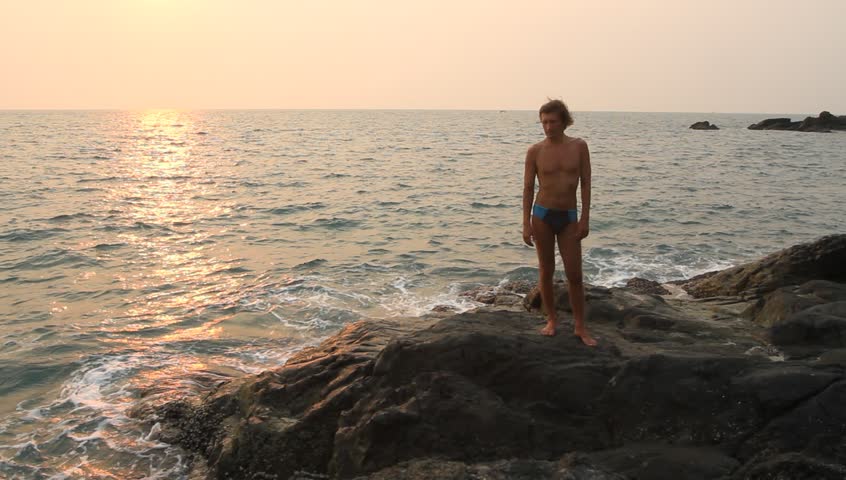 HD: Man doing yoga exercise on the deserted wild stone sea beach.