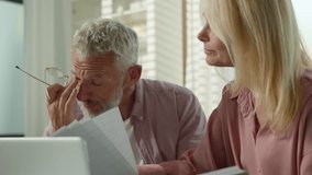 Tired pensive Caucasian couple family grandparents senior mature female woman elderly retired male man talk about business working with documents utility papers bills bank payment laptop sofa at home - Powered by Shutterstock - Get 15% off with code: PIKWIZARD15