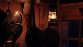 A kerosene lantern casts a warm glow over a rustic kitchen, highlighting metal pots and lids hanging on the wooden wall. The scene evokes a cozy, old-world atmosphere. - Powered by Shutterstock - Get 15% off with code: PIKWIZARD15