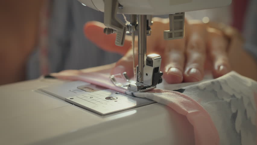 Workshop. White Asian woman using sewing machine while developing collection concept. Modern lady following fashion trends while sewing new dress model. Close-up of sewing needle movement