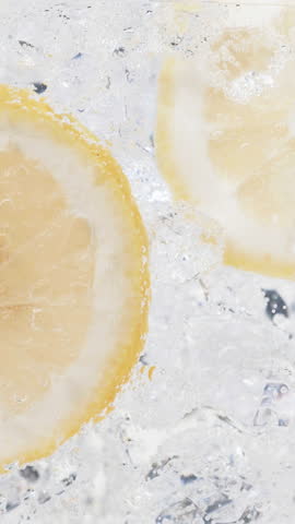 Soda water with ice cubes and sliced lemon slow motion vertical video.