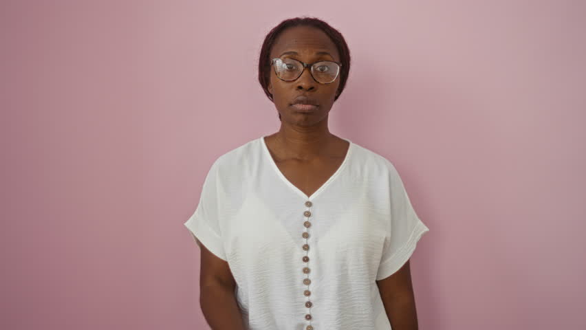 Secretive young african american woman with glasses standing over isolated pink background, mouth zipped shut, lips closed with finger gesture in silent confidence