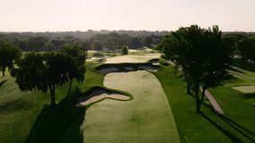 an aerial drone shot moving down to show a beautiful golf hole during sunrise, it's fairways, green, and bunkers - Powered by Shutterstock - Get 15% off with code: PIKWIZARD15