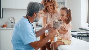 Elderly male pediatrician plays with a small child using a teddy bear, a smiling little girl who came for a medical examination with her mother at the doctor's hospital - Powered by Shutterstock - Get 15% off with code: PIKWIZARD15