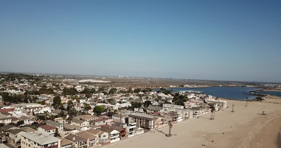 aerial footage of the silky brown sand and vast blue ocean water at the beach with people relaxing in the sand and homes and apartments along the beach at Seal Beach in Seal Beach California USA