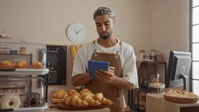 Young man with a beard in a bakery holding a tablet surrounded by pastries and shelves in the background - Powered by Shutterstock - Get 15% off with code: PIKWIZARD15