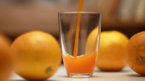 Freshly squeezed orange juice is poured into a clear glass on a table next to whole oranges, captured in a close-up shot. - Powered by Shutterstock - Get 15% off with code: PIKWIZARD15