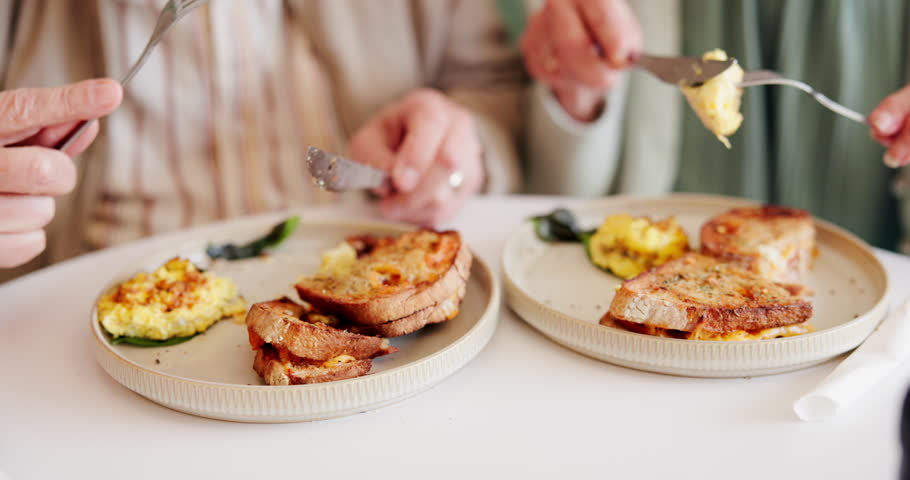Hands, eating and breakfast in restaurant for relax, relationship and morning with eggs, bacon and toast. Elderly people, hungry and food in cafe for nutrition, brunch or bonding with closeup on date