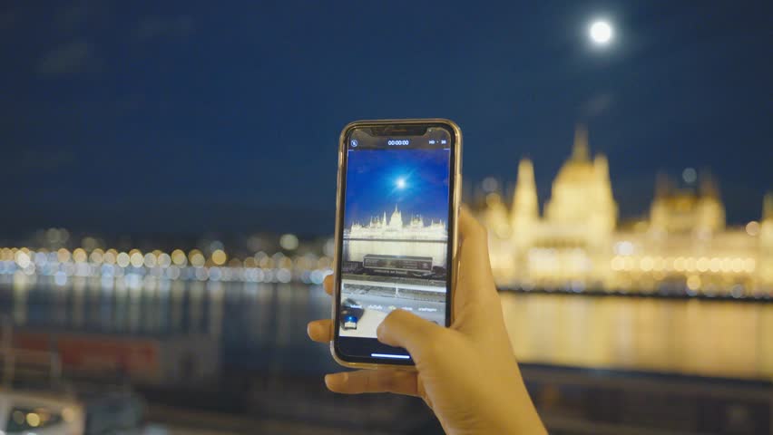 A large building with a yellow facade is lit up at night. The building is surrounded by a street with a few people walking around