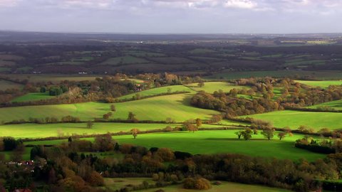 Stunning aerial shot over lush green fields and meadows in the English countryside. It is a clear, bright autumn day and the sun is shining.