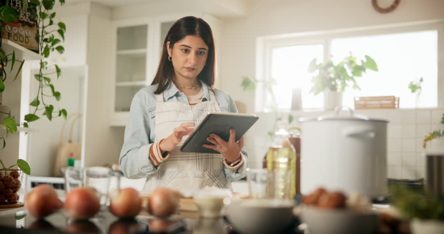 Food, recipe and tablet with woman in kitchen of home for cooking ingredients or instructions on internet. Apron, preparation and search with Indian person in apartment for diet, health or nutrition