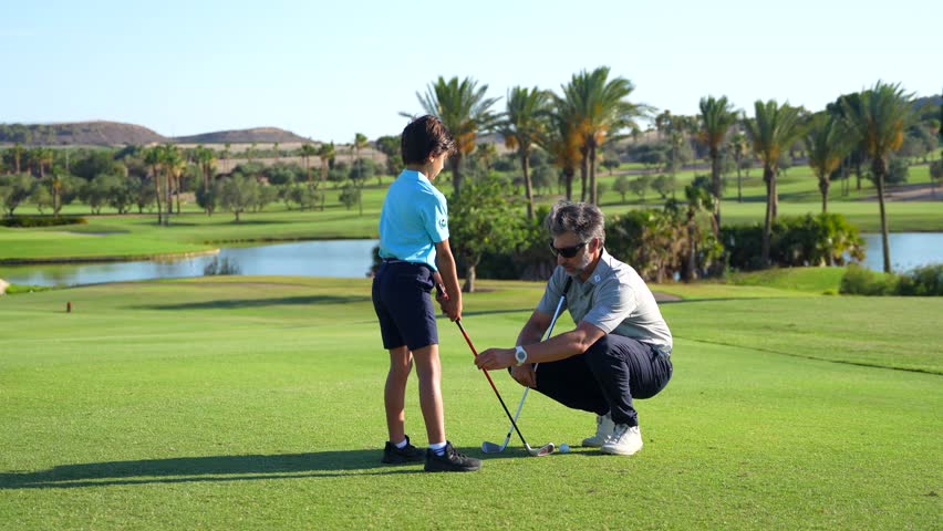 Male adult caucasian instructor correcting and guiding a boy during golf lesson in a green luxury course - Powered by Shutterstock - Get 15% off with code: PIKWIZARD15