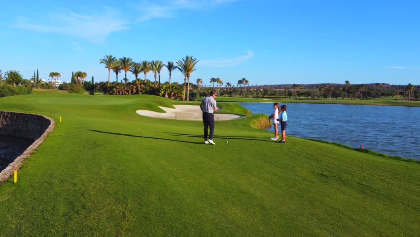 Male mature instructor teaching a girl how to play golf next to a boy in a luxury green gold course - Powered by Shutterstock - Get 15% off with code: PIKWIZARD15
