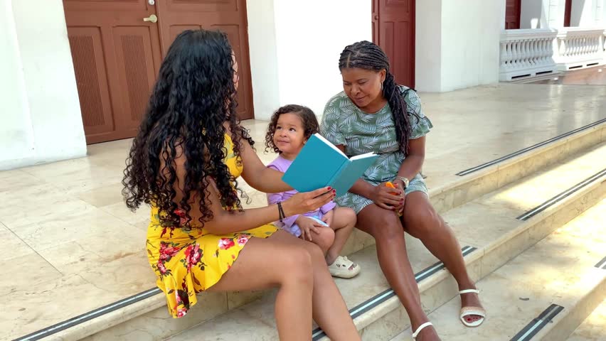 Three generations of women enjoying a storybook on the steps outside, sharing a special moment.