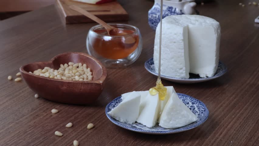 Fresh honey and homemade ricotta cheese. Pine nuts in heart-shaped plate. Wooden and vintage dishes and food on table. Healthy natural breakfast. 
