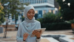 Happy Attractive Muslim Woman Walking Outside Using the Digital Tablet Scrolling Apps, Social Media. Young Pretty Female Going Home and browsing in the Digital Device, Swiping Pics. - Powered by Shutterstock - Get 15% off with code: PIKWIZARD15