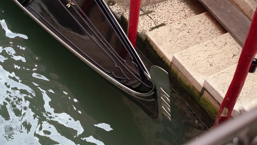 A black gondola parked on a canal with no people inside.