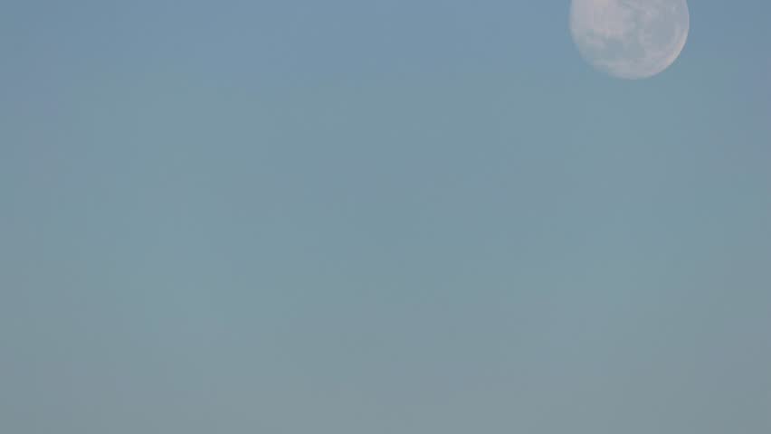 Timelapse telephoto view of full moon setting in blue sky, copy space left