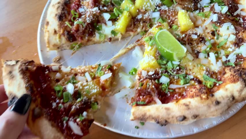 Pulling pizza slice from carne asada pizza with pineapples, limes, Oaxacan cheese, red sauce, onions, and more. Delicious pizza pie cheese pull  