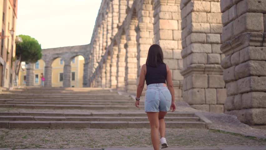 Aqueduct of Segovia visited by girl travelling to Spain walking arround this artichetectural structure which is considered as a world heritage.
