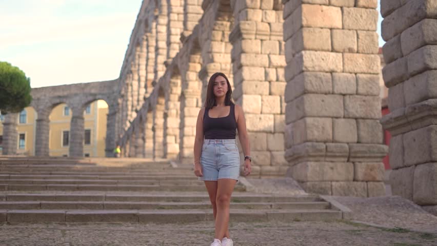 Aqueduct of Segovia visited by girl travelling to Spain walking arround this artichetectural structure which is considered as a world heritage.