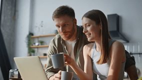 Laughing spouses watching laptop at calm family morning closeup. Smiling couple drinking coffee in kitchen looking computer screen. Happy romantic couple enjoying hot beverage talking together at home - Powered by Shutterstock - Get 15% off with code: PIKWIZARD15