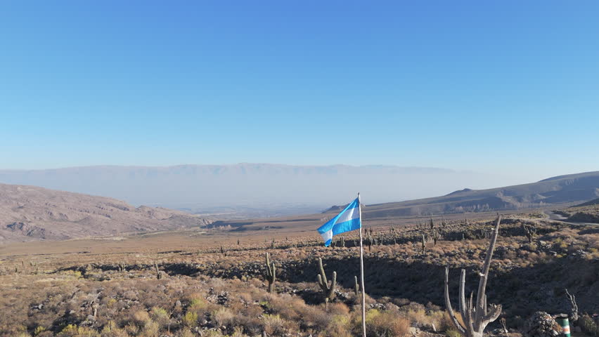 A beautiful drone image of the Argentine flag waving in the wind in the mountainous region of Amaicha del Valle, nestled within the Andes Mountains.