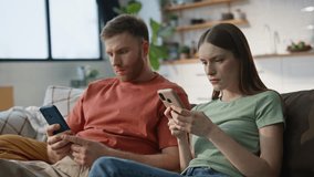 Worried wife showing message smartphone to husband sitting together at couch living room closeup. Concerned married couple looking cellphone reading bad news at home. Frowned girlfriend receiving sms. - Powered by Shutterstock - Get 15% off with code: PIKWIZARD15