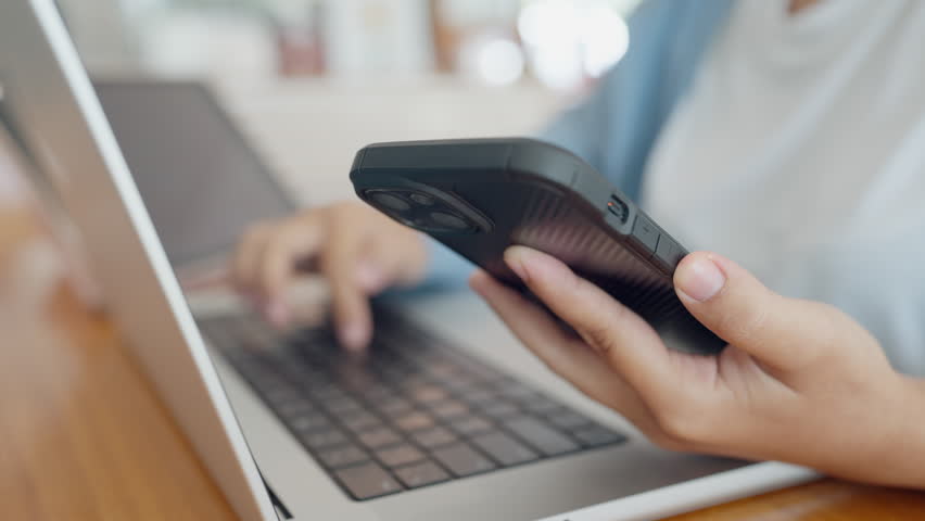 A woman is using a laptop and a cell phone