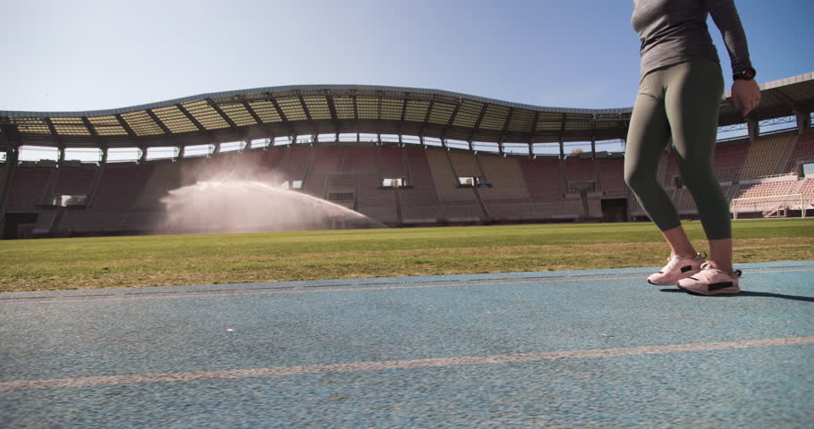 Sports girl running. Runner on a synthetic track at generic open stadium. Water irrigation in the backgorund.