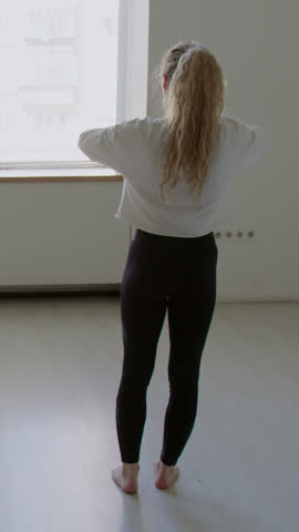 Vertical back view shot of fit female dancer doing standing hip circles while warming up before studio rehearsal