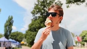 Young man with sunglasses eats an ice cream waffle cone, walking among green trees. Slow motion. - Powered by Shutterstock - Get 15% off with code: PIKWIZARD15
