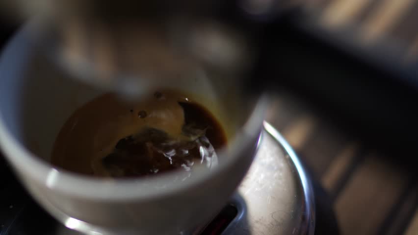 Black coffee dripping from a coffee maker horn into a cup on a tray