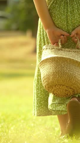 Little blonde girl in green dress walks on a lawn in the park on a summer day, vertical video