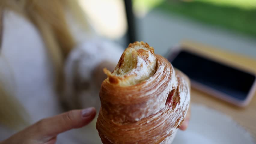 A close-up of a girl taking an appetizing bite of a croissant and chewing. Top view. Croissant breakfast.