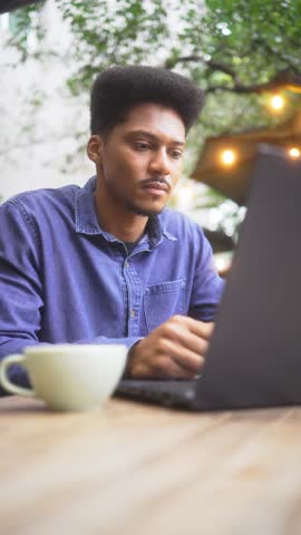 Focused Young Professional Drinking Coffee and Working on Laptop in outdoor, cafe, African American Man Concentrating in Cozy, Peaceful Setting