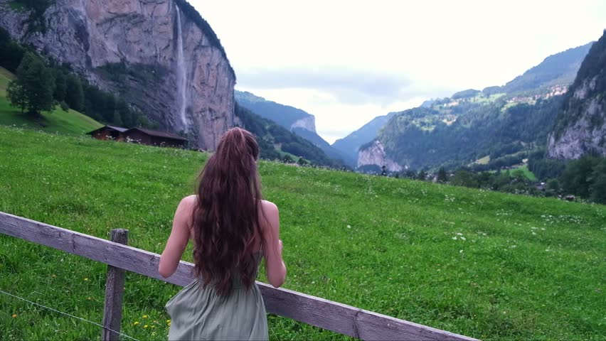 A girl with long curly hair in a green dress against a beautiful background of a waterfall mountain in Switzerland