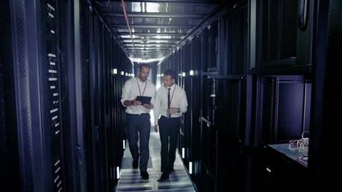 Team of people working in a data center with rows of server racks and super computers. They are looking into data cabinets and checking cables and other equipment.