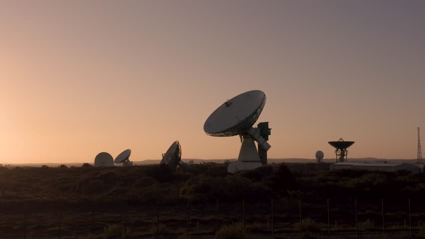 4K aerial footage of a large satellite dish broadcasting signals into deep space from earth to discover new life with dramatic sunset