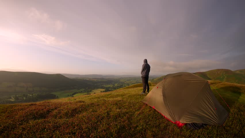 A man camping in beautiful British countryside. He is standing outside his tent