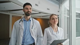 Medical team going hospital hallway closeup. Happy doctors in white uniform walk healthcare center. Smiling bearded doctor with stethoscope greet waving hand at colleague. Professional clinical staff - Powered by Shutterstock - Get 15% off with code: PIKWIZARD15
