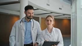 Smiling medics discussing diagnosis walking together. Closeup happy doctors work reviewing patient chart in hospital hallway. Professional medical staff go modern center. Confident man consult nurse - Powered by Shutterstock - Get 15% off with code: PIKWIZARD15