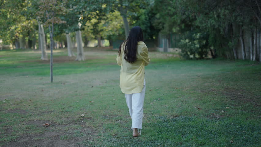 Young brunette Caucasian girl walking barefoot through the grass towards the camera smiling with an LGTBI flag on her back