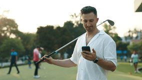 Portrait of bearded man with golf club looking at cellphone screen on sports ground. Male player reads news about competition winners in social media. Positive golfer bets online - Powered by Shutterstock - Get 15% off with code: PIKWIZARD15