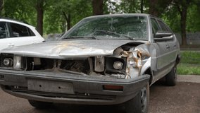 Tracking shot of destroyed abandoned car with heavily damaged front part, rusting away on side of street on cloudy summer day, evoking a sense of decay and neglect. Shooting in slow motion. - Powered by Shutterstock - Get 15% off with code: PIKWIZARD15
