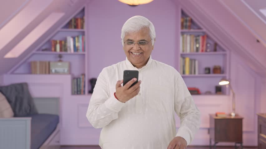 Happy Indian old man scrolling through phone