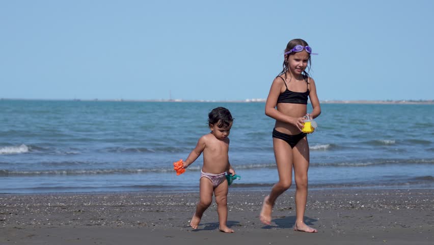 Two children playing with toys on sandy beach. Little sisters having fun on..