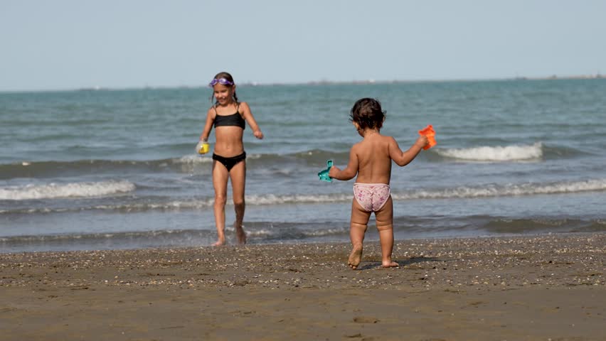 Two children playing with toys on sandy beach. Little sisters having fun on..