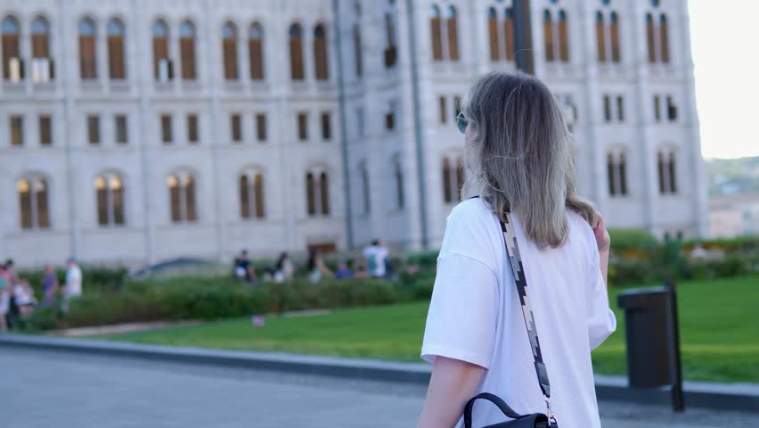 Young adult woman walk through Budapest squares tourist spot in Hungary. Caucasian woman navigating through square of Budapest city elegant buildings and lively atmosphere in Hungary.