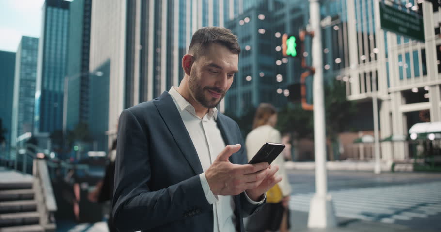 Handsome Man in a Business Suit Standing on a Busy City Sidewalk, Holding His Smartphone. Young Man Reviewing His Work Schedule and Responding to Emails as He Commutes to Work